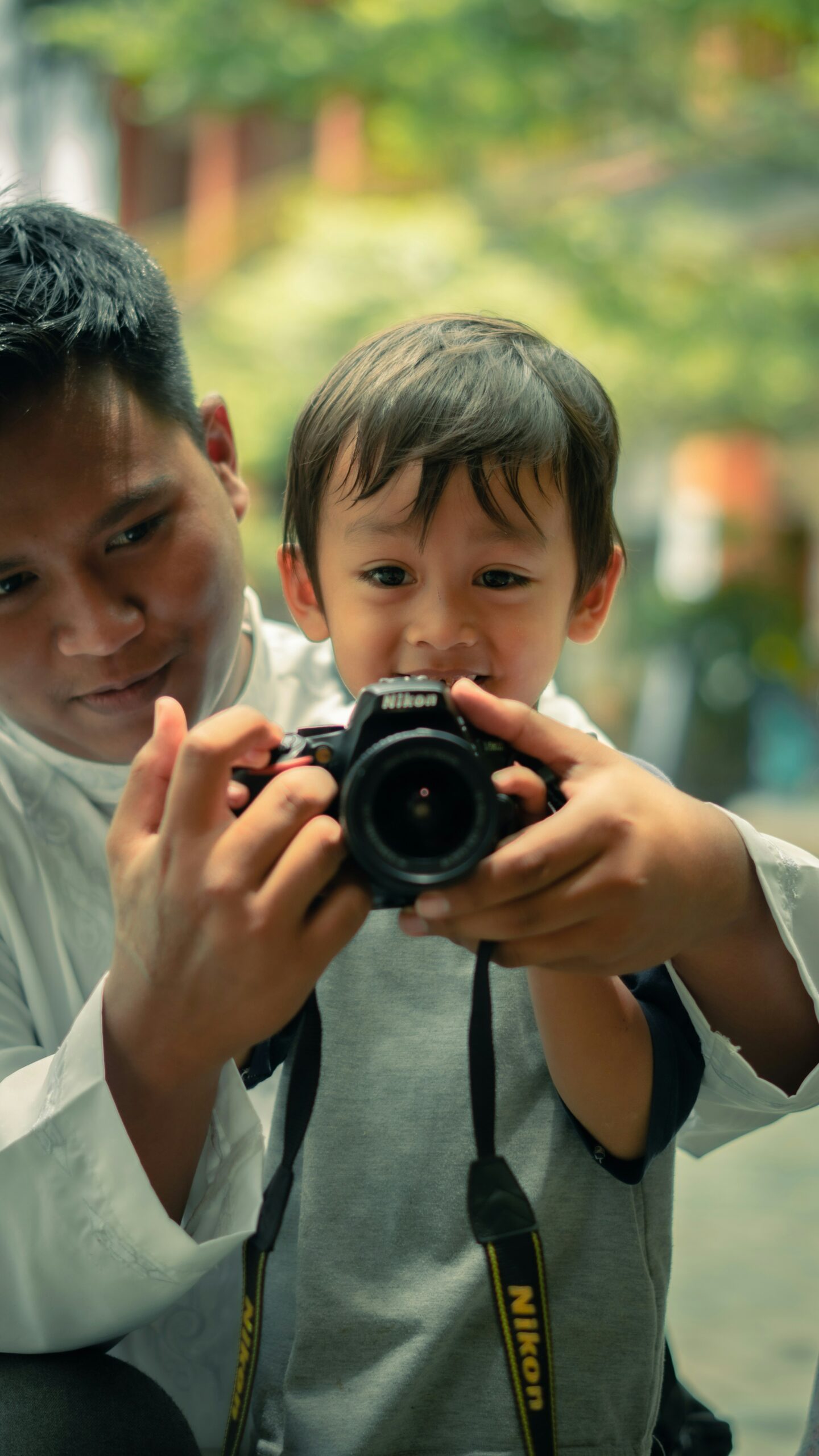 muhammad-azzam-mYUeSNr_guw-unsplash Un papa aide son petit garçon dans ses bras à se servir d'un appareil photo